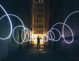 Silhouette of person making circles with flashlight on dark street