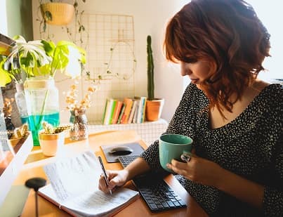 woman writing on her notebook while holding a cup