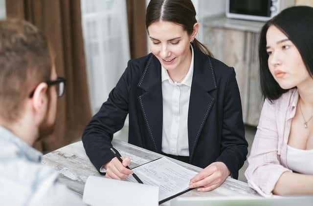 Insurance officer behind his desk explaining insurance policy to two women