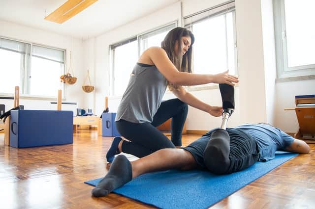 female physical therapist helping a man flexing his bionic leg on the floor on a mat